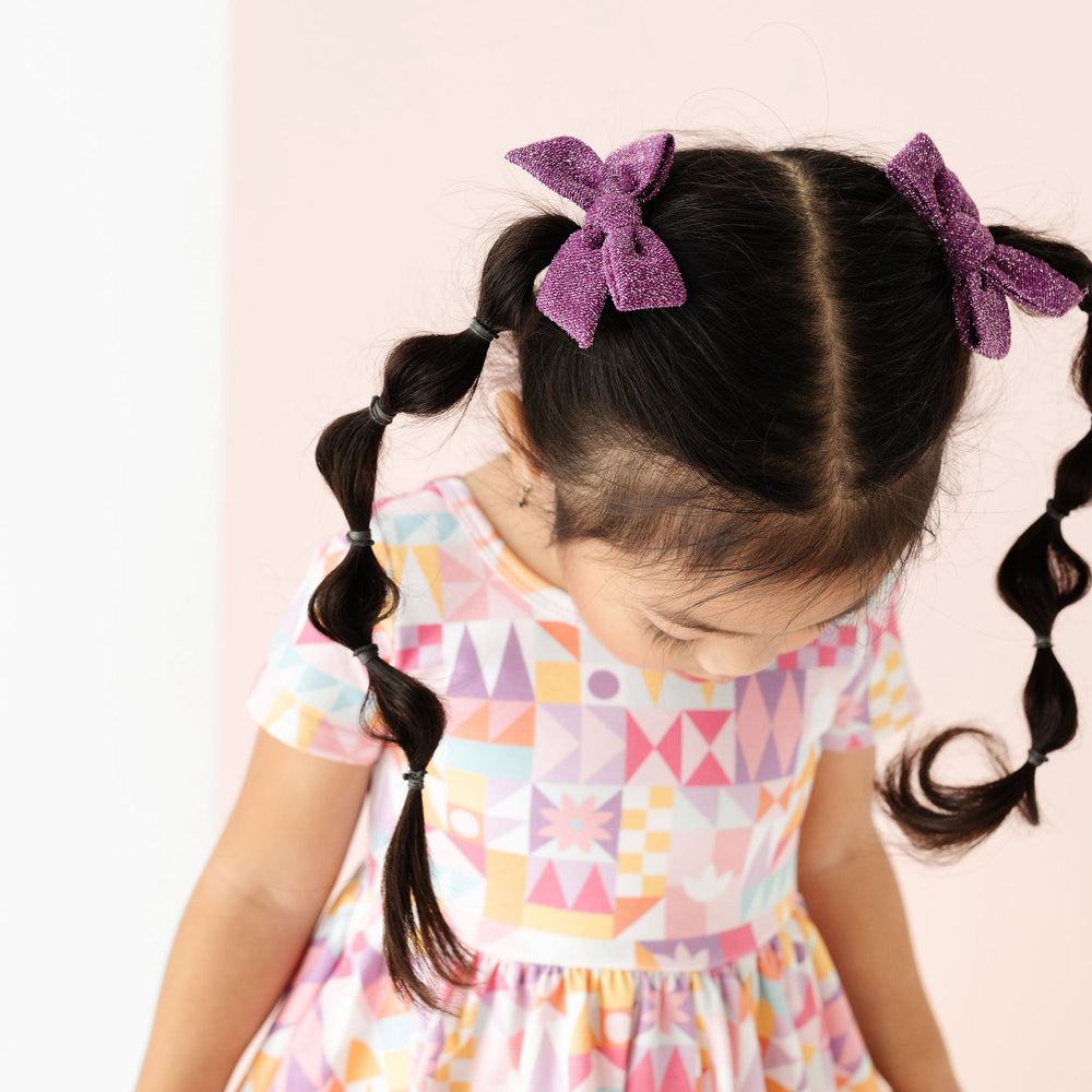 sparkly purple pigtail bows on little girl wearing geometric print disney inspired dress