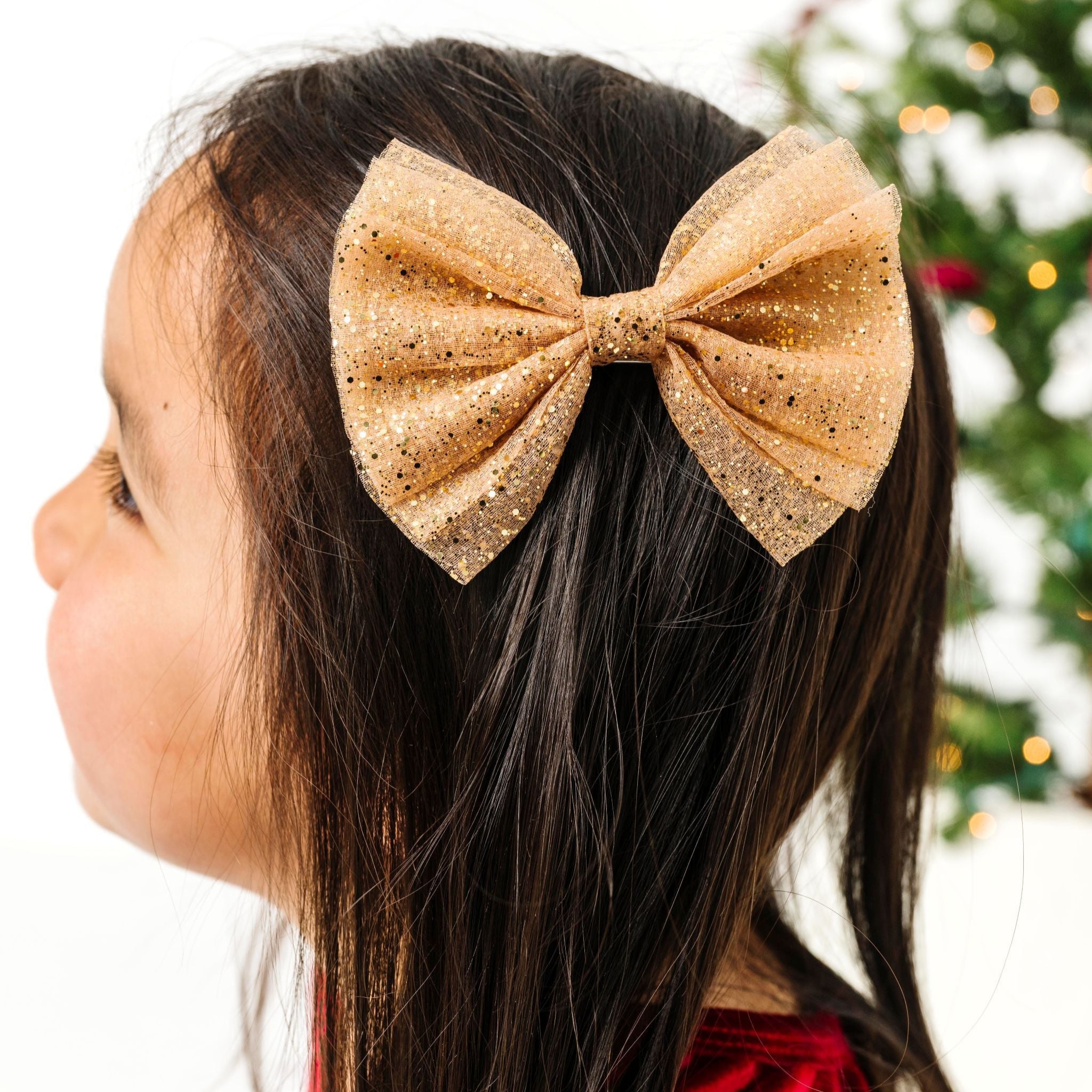 little girl in front of Christmas tree in sparkly gold tutu bow on clip paired with red velvet Christmas dress
