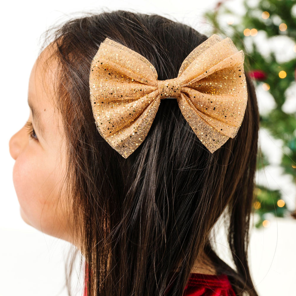 little girl in front of Christmas tree in sparkly gold tutu bow on clip paired with red velvet Christmas dress