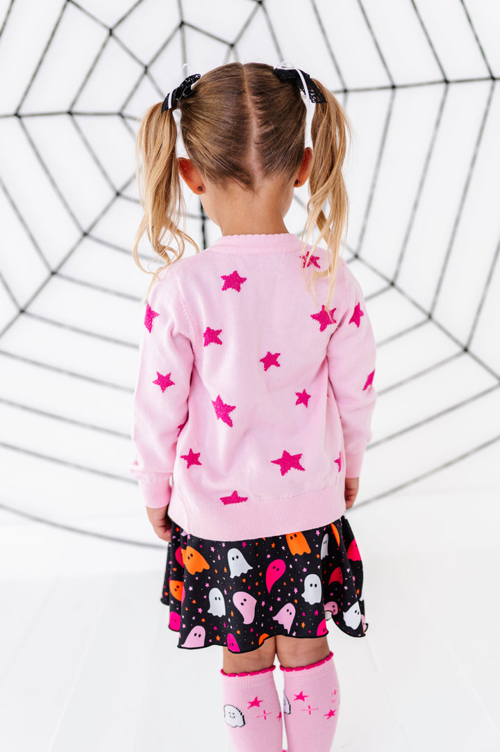 little girl facing spider web wall deco in light pink sweater with sparkly pink star design and matching ghost dress and knee socks