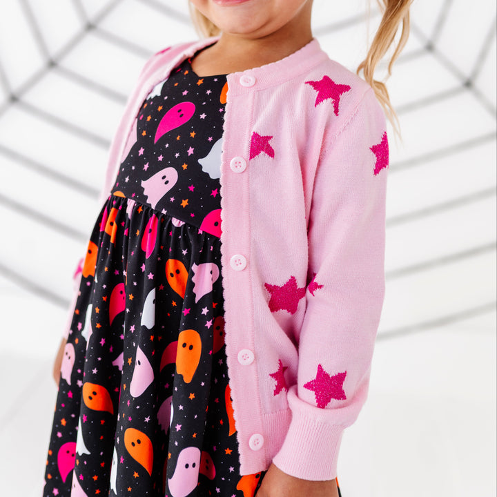 closeup of light pink cardigan with sparkly hot pink star design paired with pink and orange ghost print Halloween dress