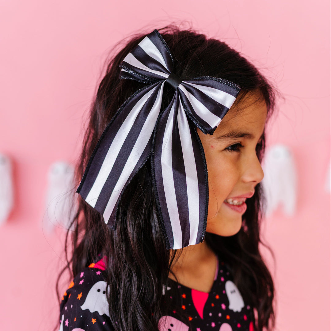 young girl wearing oversized black and white satin hair bow on clip paired with ghost print Halloween twirl dress