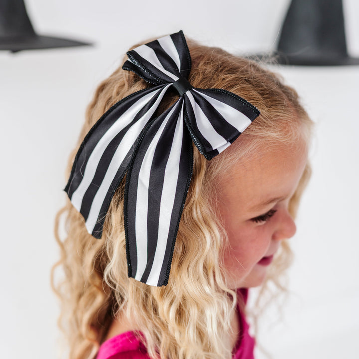 young girl with black and white striped hair bow paired with hit pink velvet twirl dress for Halloween