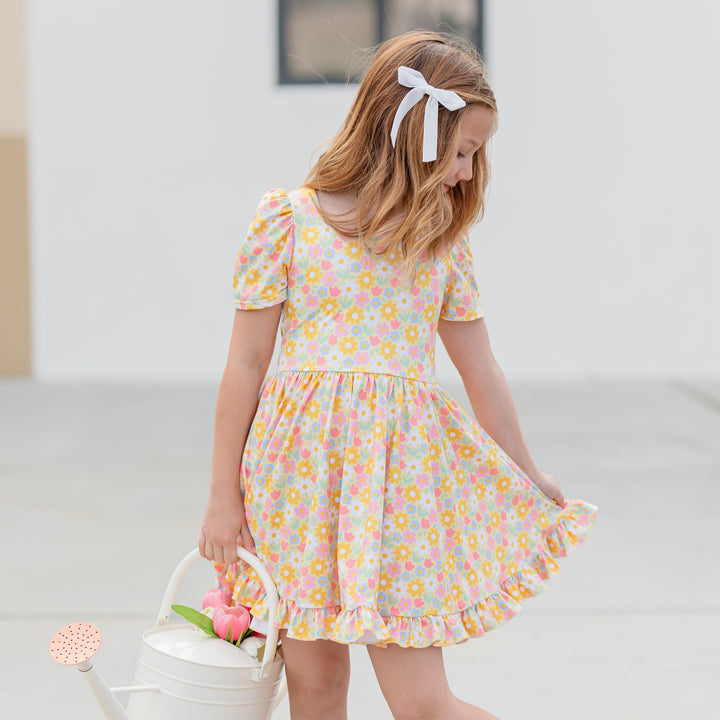 girl wearing pastel yellow square neck twirl dress with spring flower print and white velvet bow