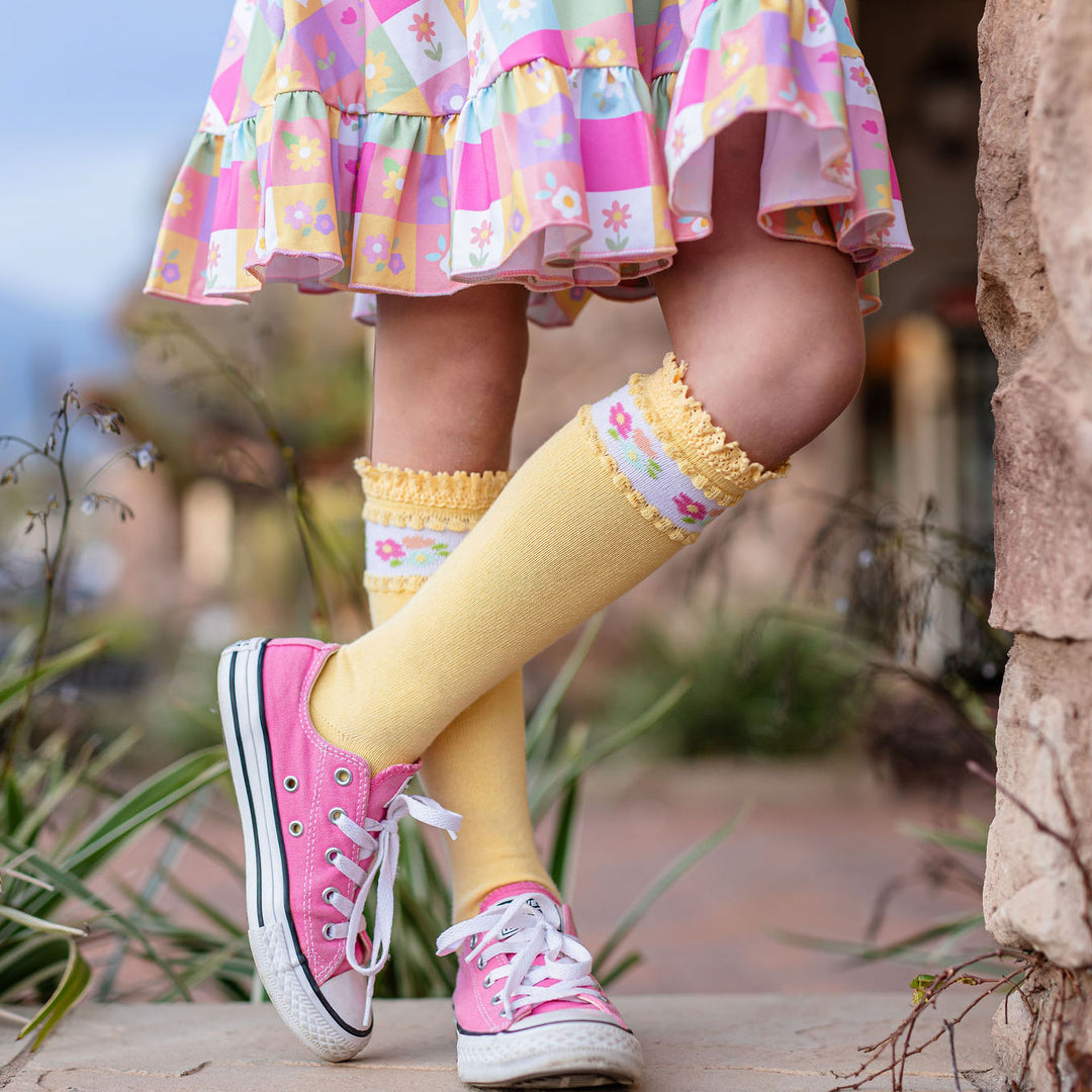 girl in flower dress and yellow lace trimmed knee high socks with floral band around top