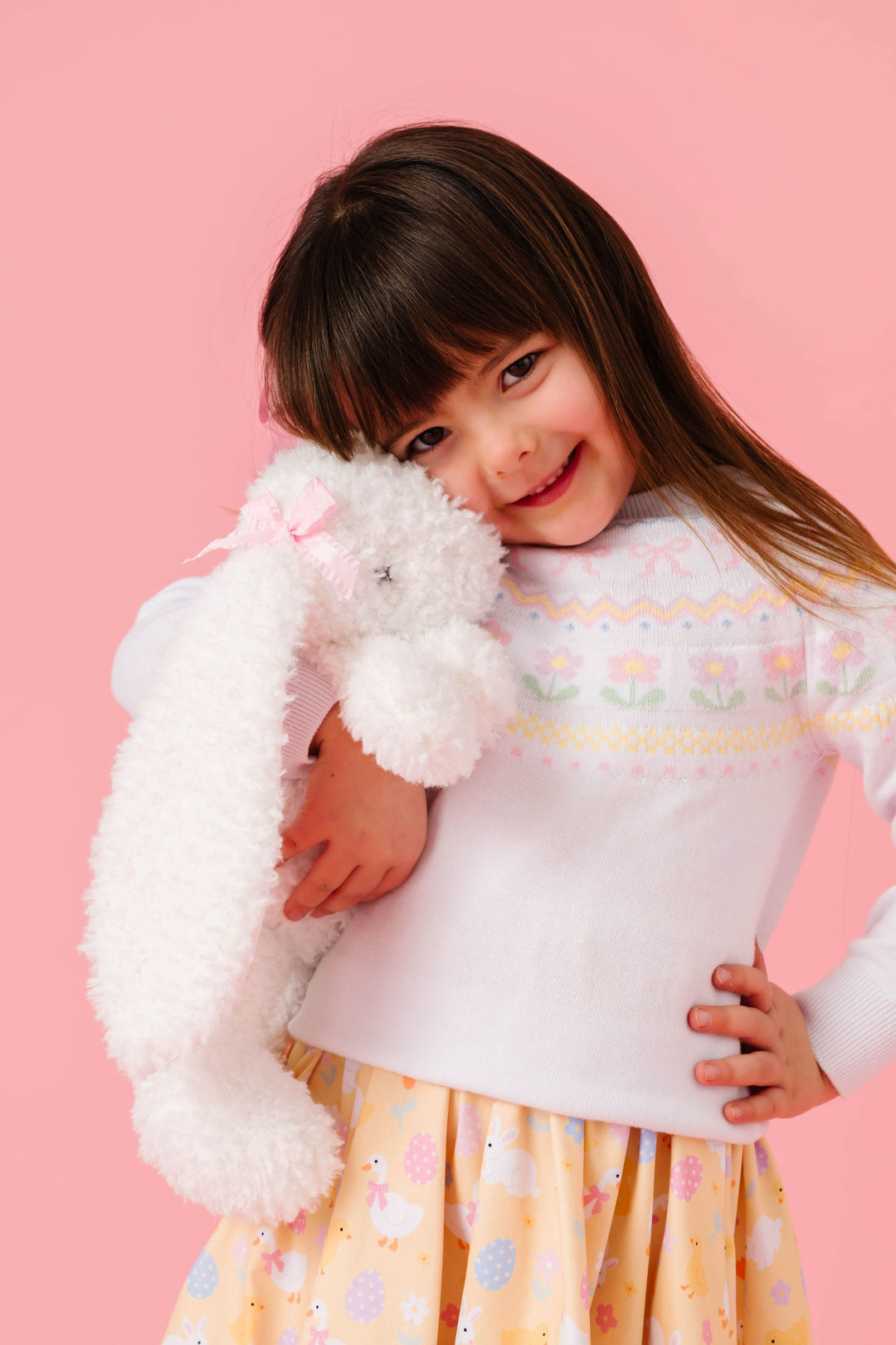 little girl hugging fluffy bunny in white sweater with spring fair isle design paired with pastel yellow Easter print dress