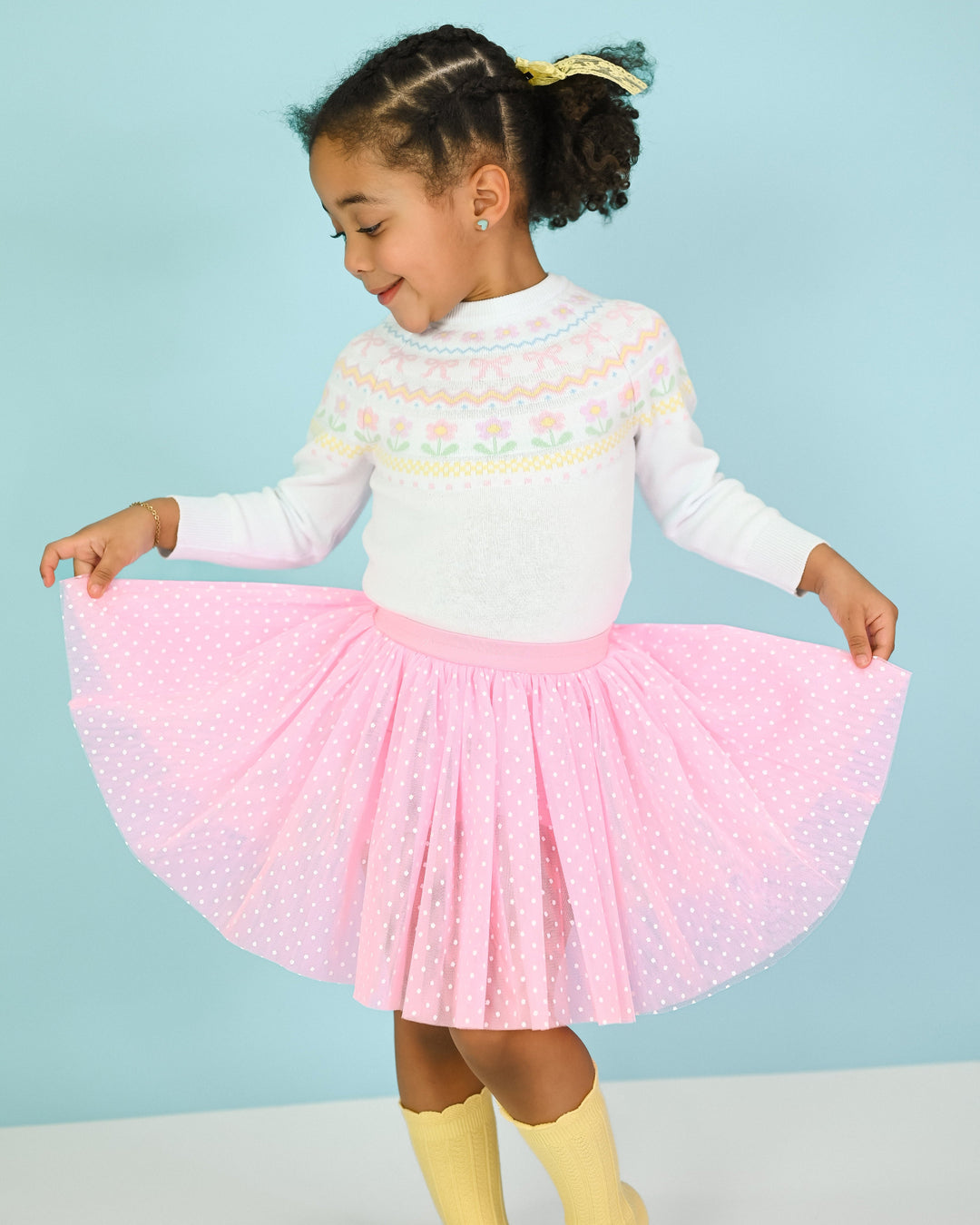 young girl in white spring fair isle sweater, pink utu skort with white dots and yellow knee socks for spring