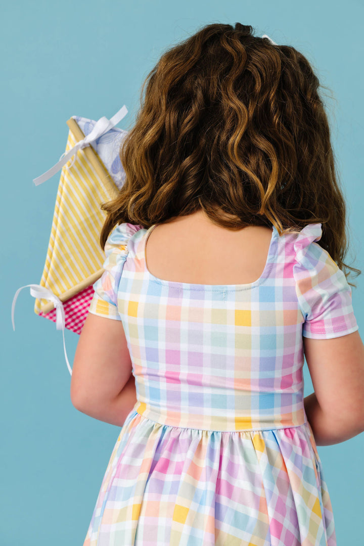 back view of little girl holding kite wearing pastel gingham print square neck twirl dress