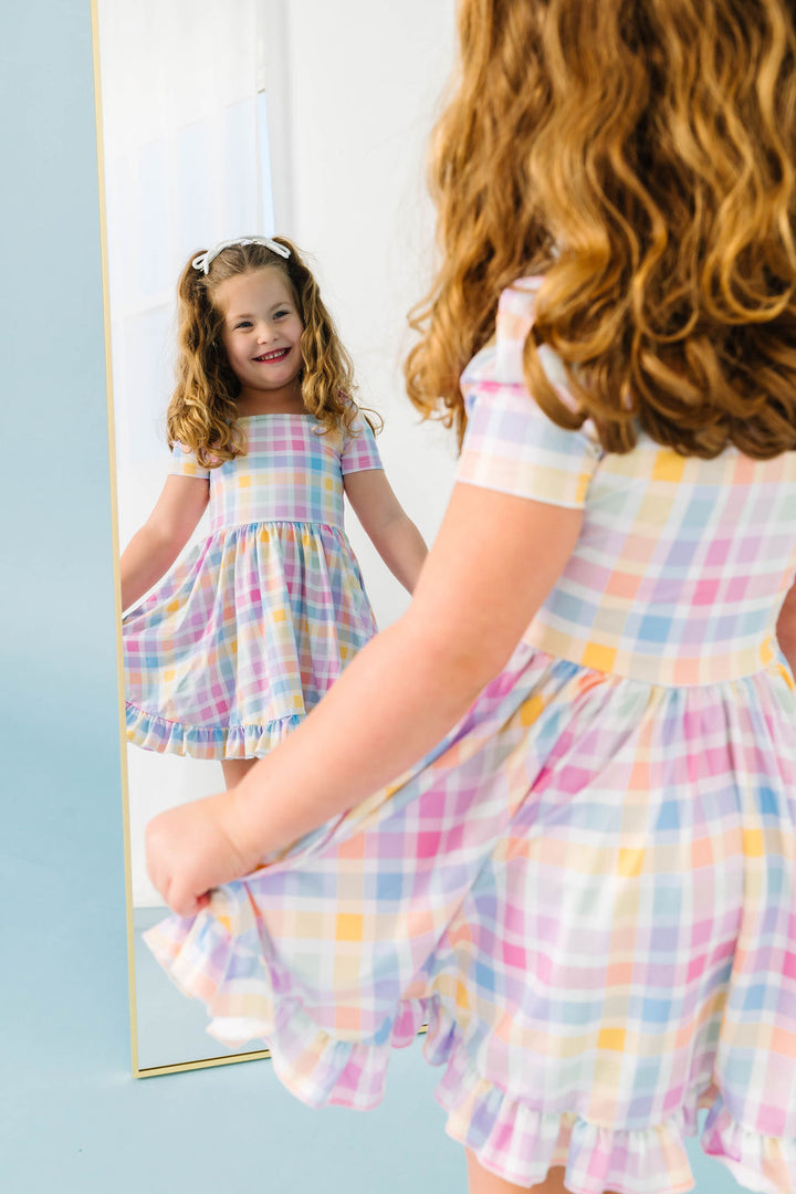 young girl looking in mirror in pastel gingham twirl dress