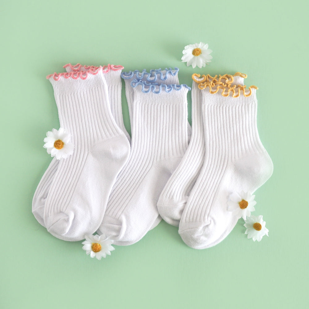 flat lay with daisies for three pairs of white ribbed midi length socks with lettuce trim in pink, blue and yellow for spring