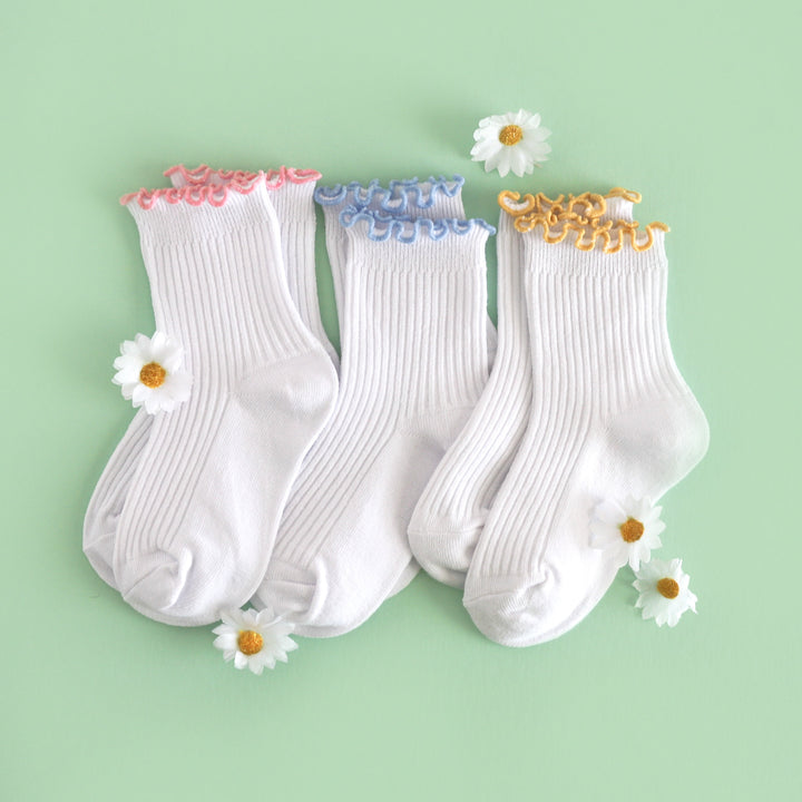 flat lay with daisies for three pairs of white ribbed midi length socks with lettuce trim in pink, blue and yellow for spring