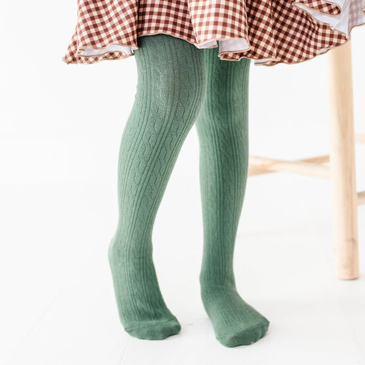 little girl in sage green cable knit tights paired with brown gingham twirl dress