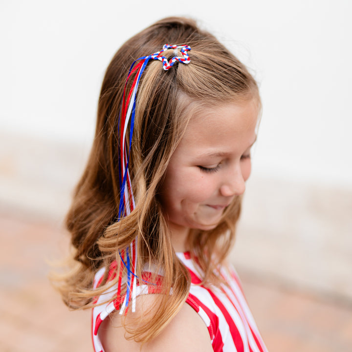 girl wearing star shaped ribbon hair clip with braided red, white and blue star and long ribbons for fourth of july