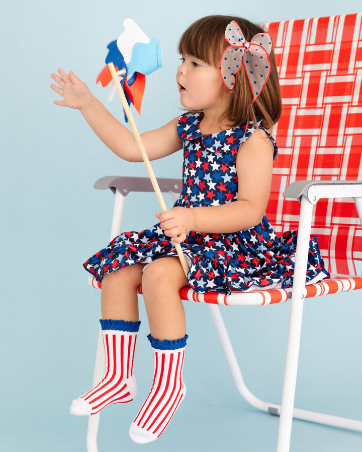 little girl holding patriotic pinwheel wearing cute 4th of july star print dress with matching red, white and blue socks & hair bow