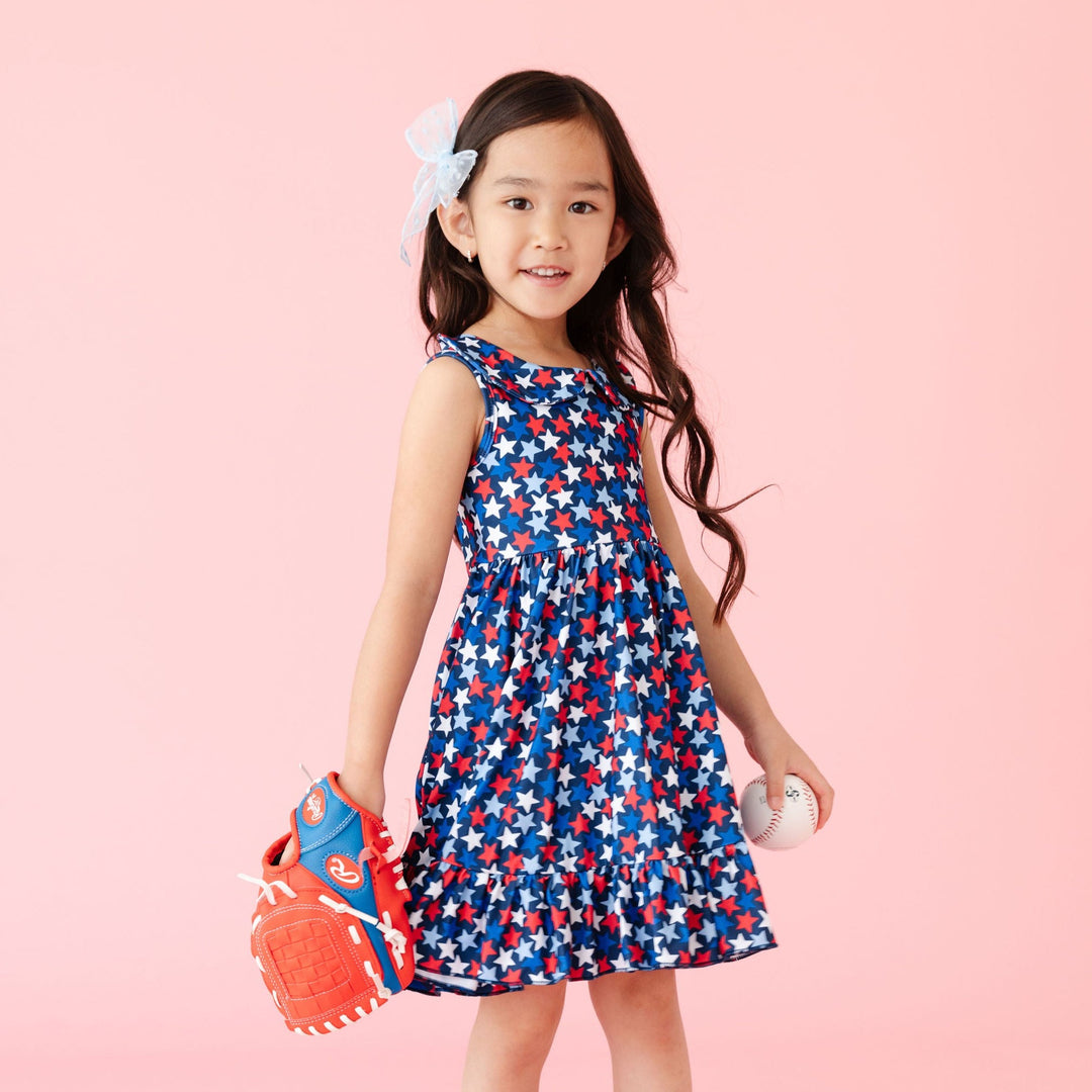 little girl holding baseball and wearing baseball glove in cute 4th of july print star dress