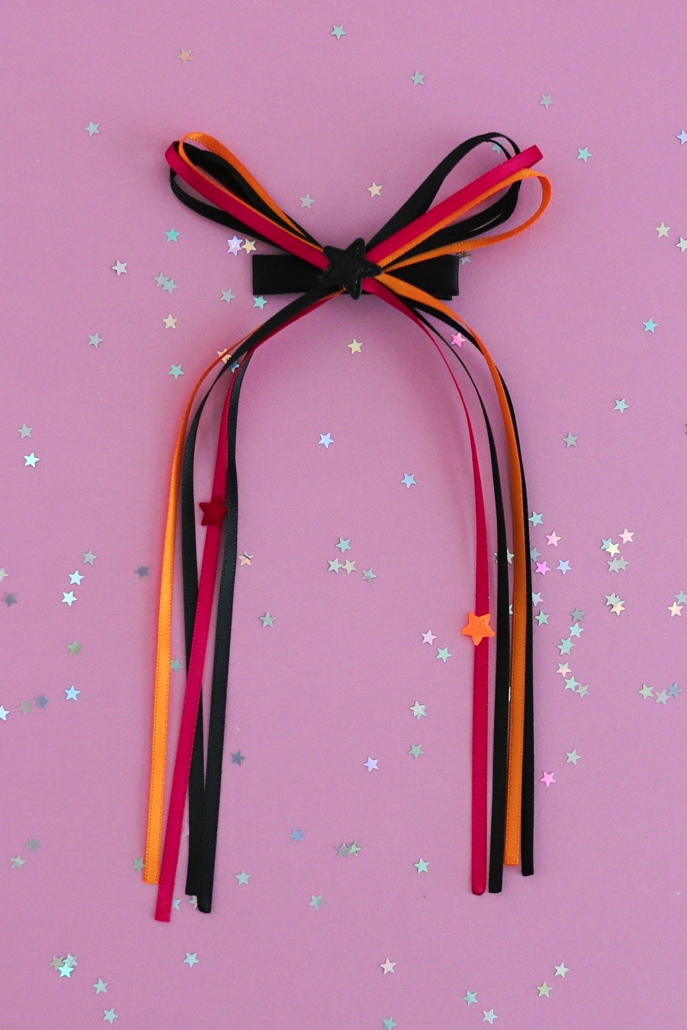 girls' Halloween ribbon streamer bow in orange, pink and black with star embellishments photographed on lavender background with star confetti