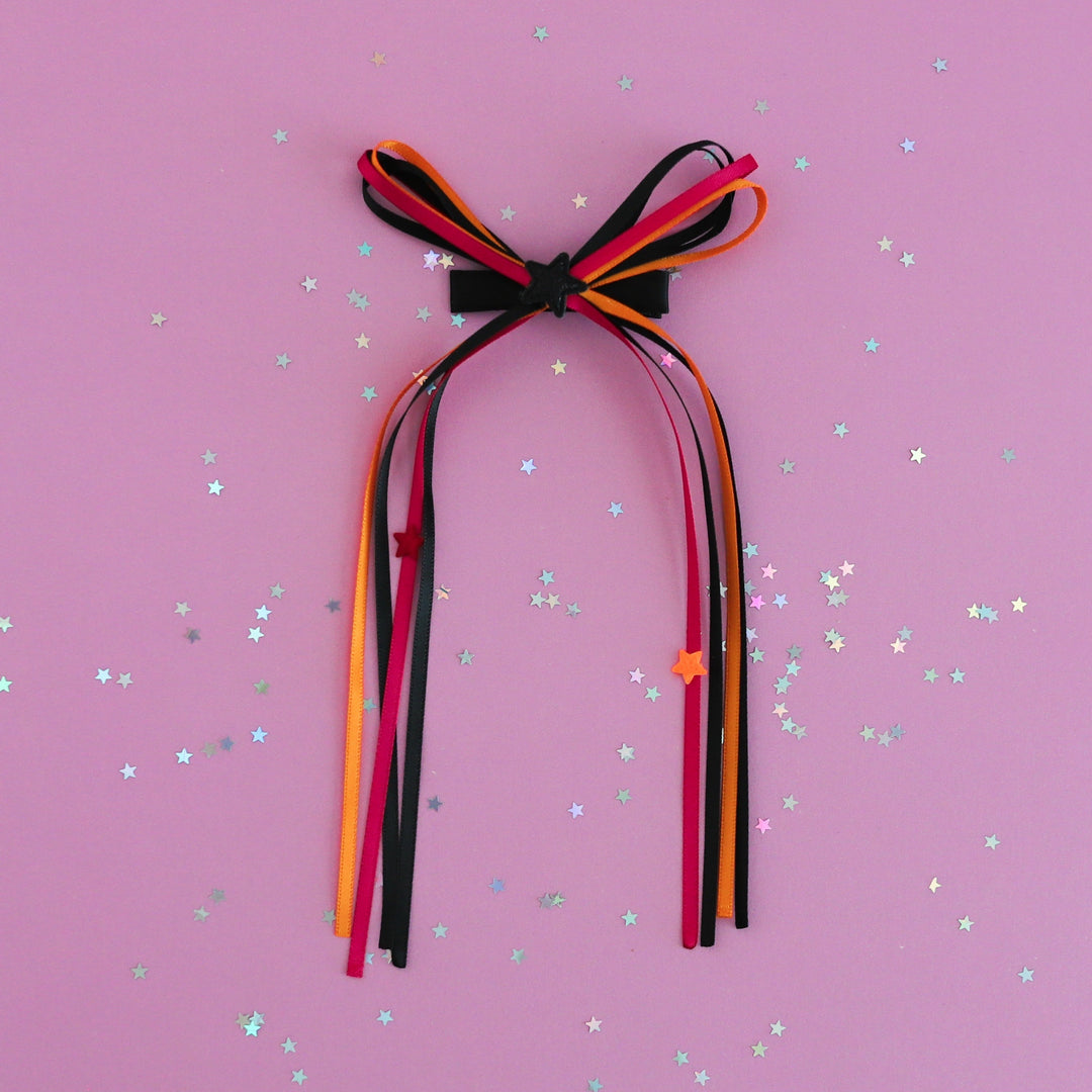 girls' Halloween ribbon streamer bow in orange, pink and black with star embellishments photographed on lavender background with star confetti