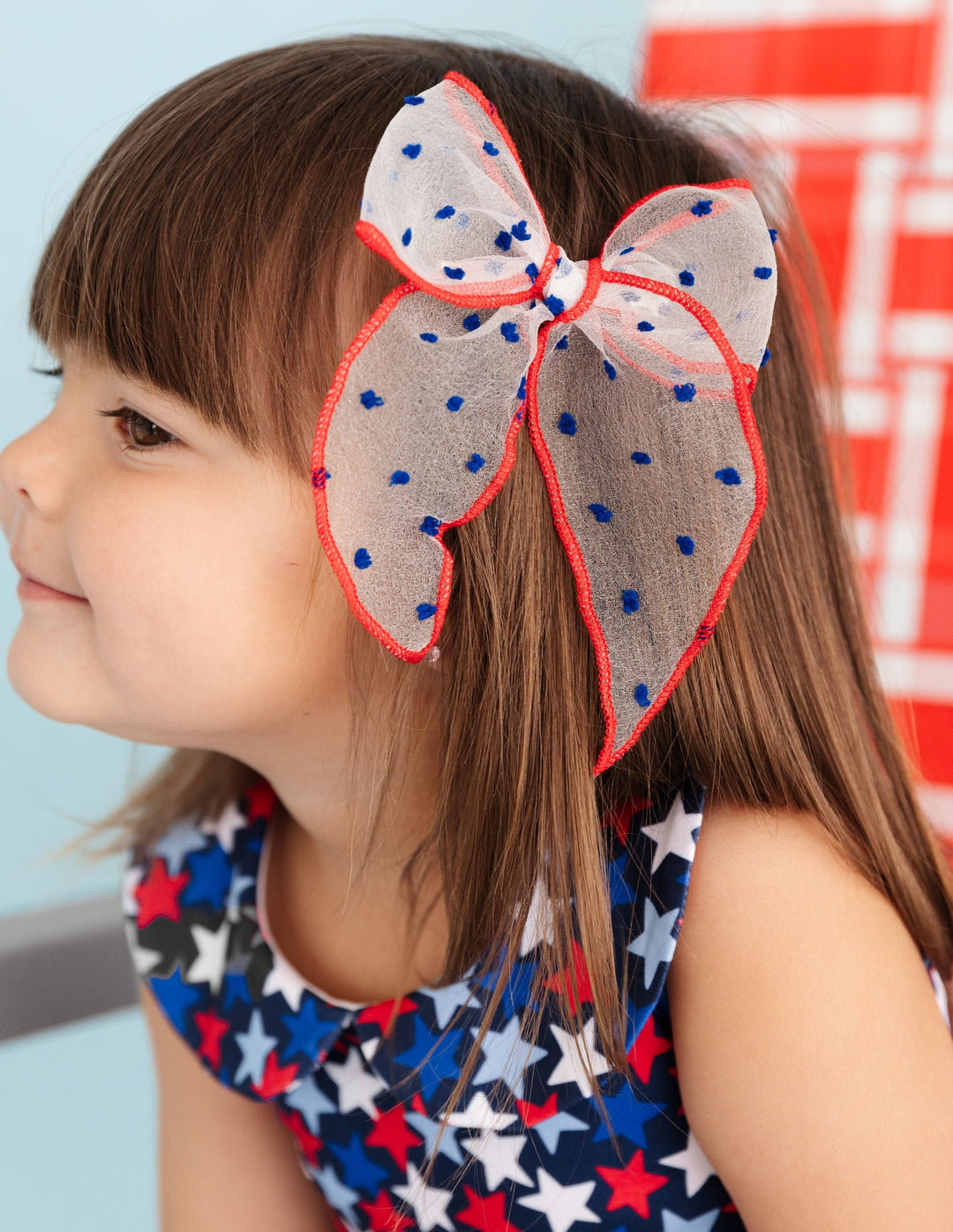 little girl wearing star print 4th of july dress with matching sheer red, white and blue dot hair bow
