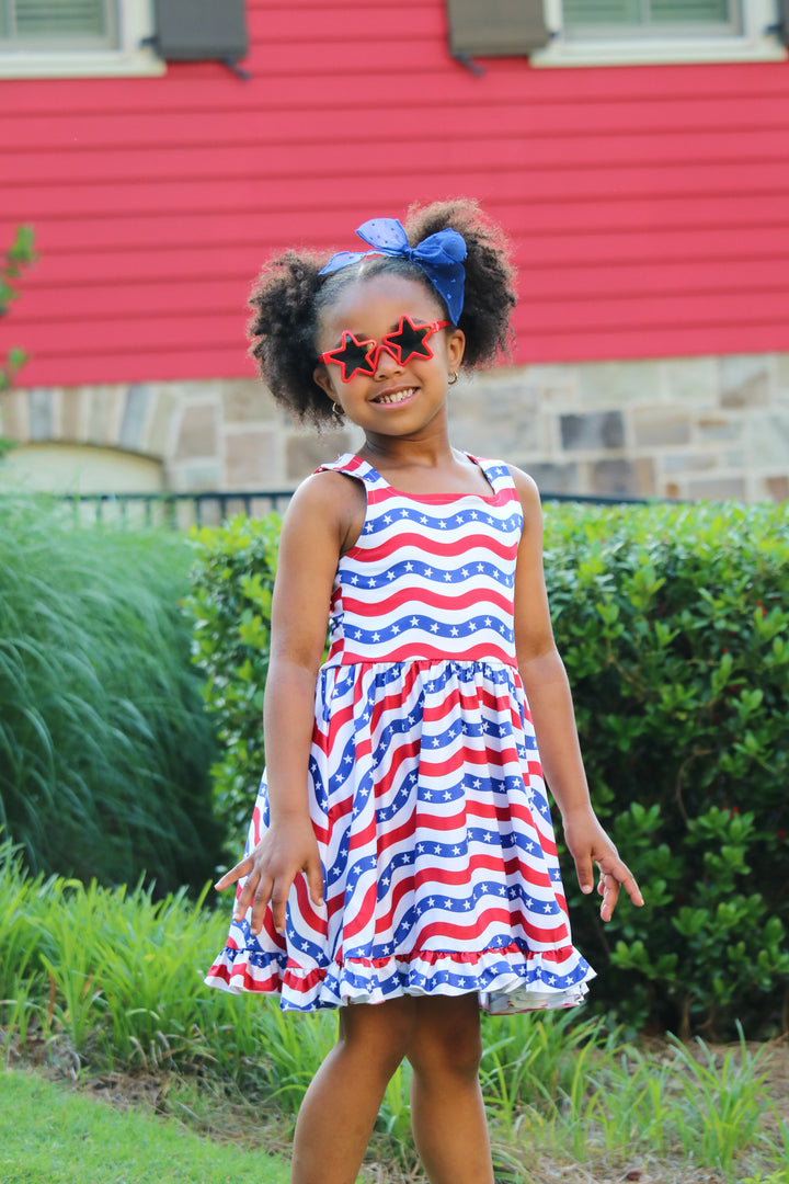 girl in 4th of july outfit with red white and blue stars and stripes dress and matching blue sheer dot bow