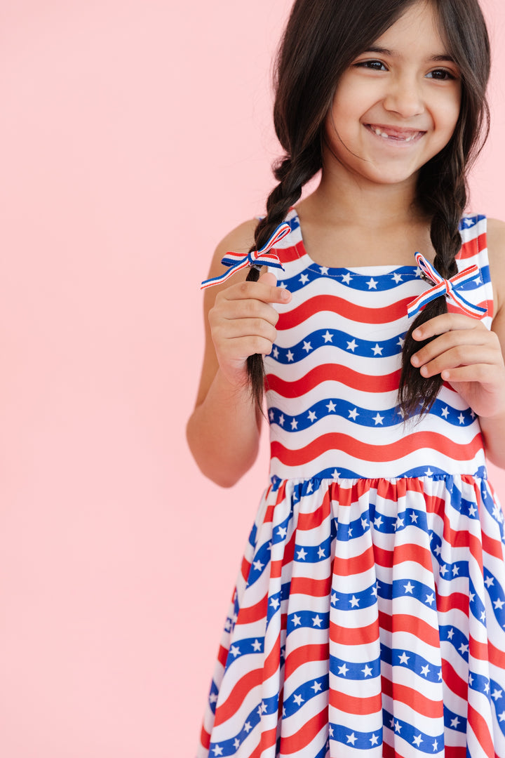 girl wearing red white and blue stars and stripes sleeveless dress and matching pigtail bows