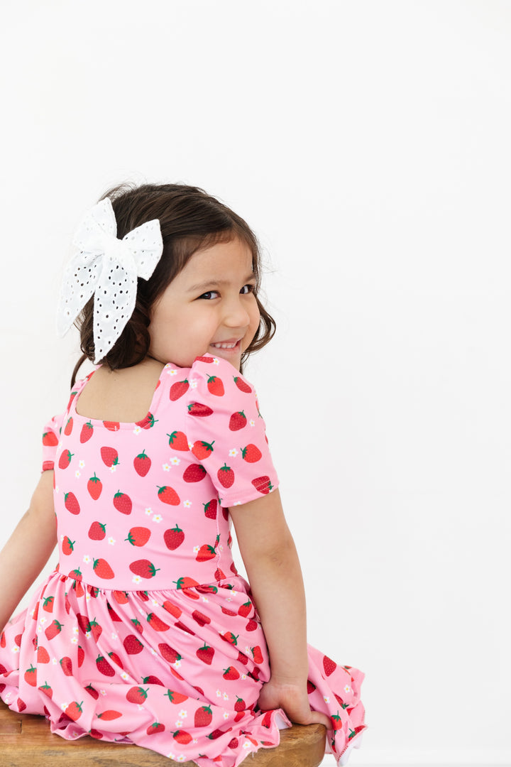 back view of pink square neck short sleeve twirl dress with red strawberry print and dainty white flowers and white eyelet bow