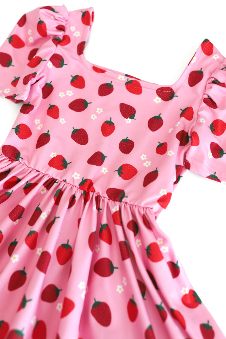 close up view of girls' pink short sleeve twirl dress with red strawberry print and dainty white flowers