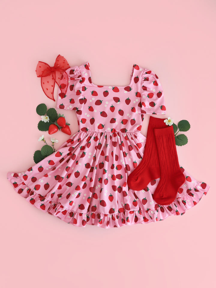 flatlay of girls' pink short sleeve twirl dress with red strawberry print and dainty white flowers with matching red socks and bows