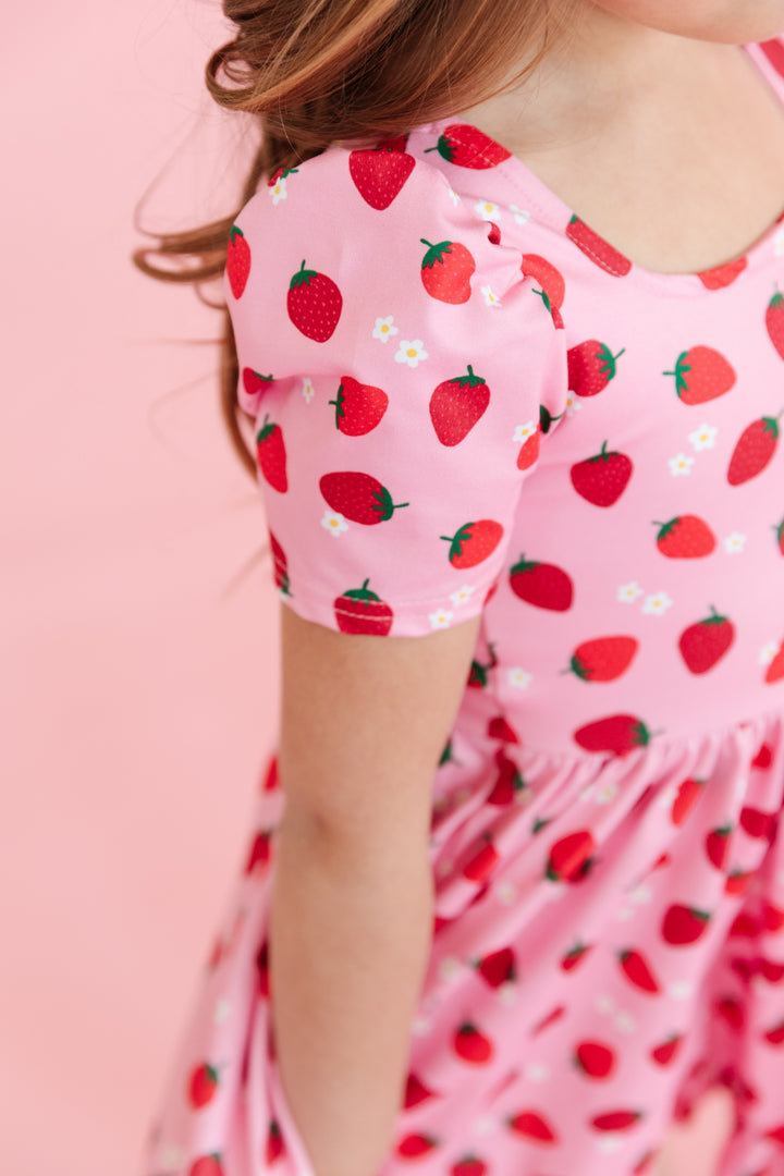 shoulder and sleeve view of pink short sleeve twirl dress with red strawberry print and dainty white flowers