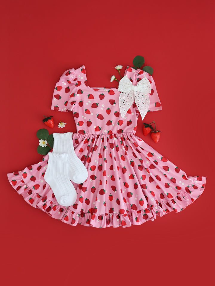 flatlay of girls' pink short sleeve twirl dress with red strawberry print and dainty white flowers and matching white frill socks and white eyelet hairbow