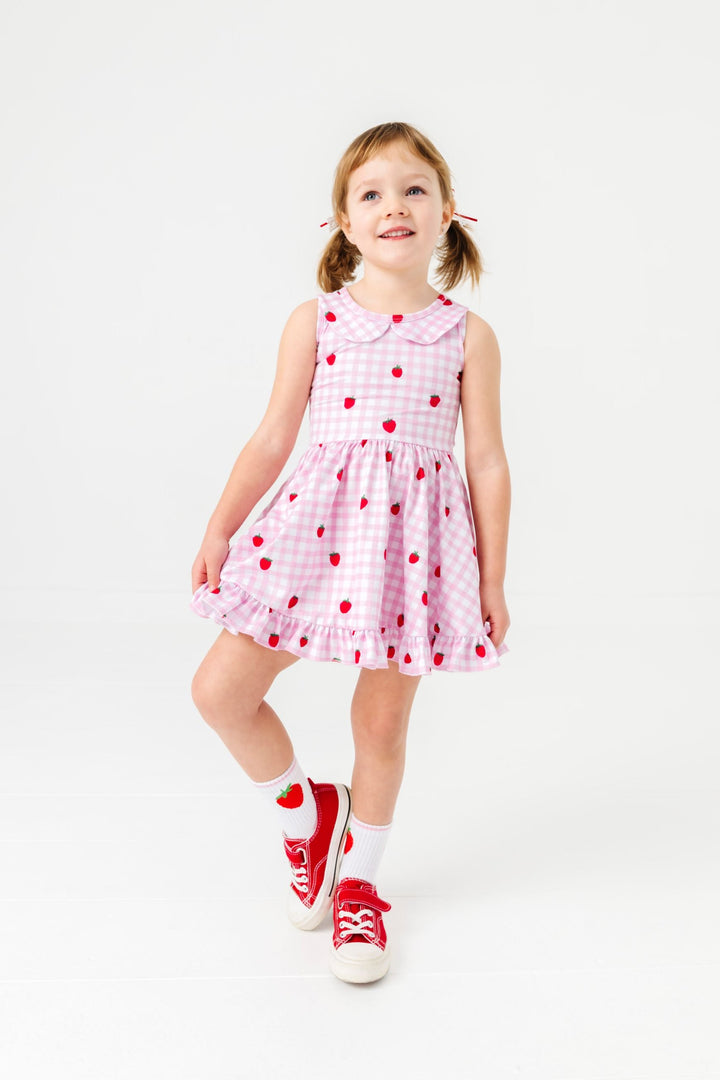 little girl in pink gingham and strawberry print sleeveless twirl dress with peter pan collar and matching white crew socks with strawberry design
