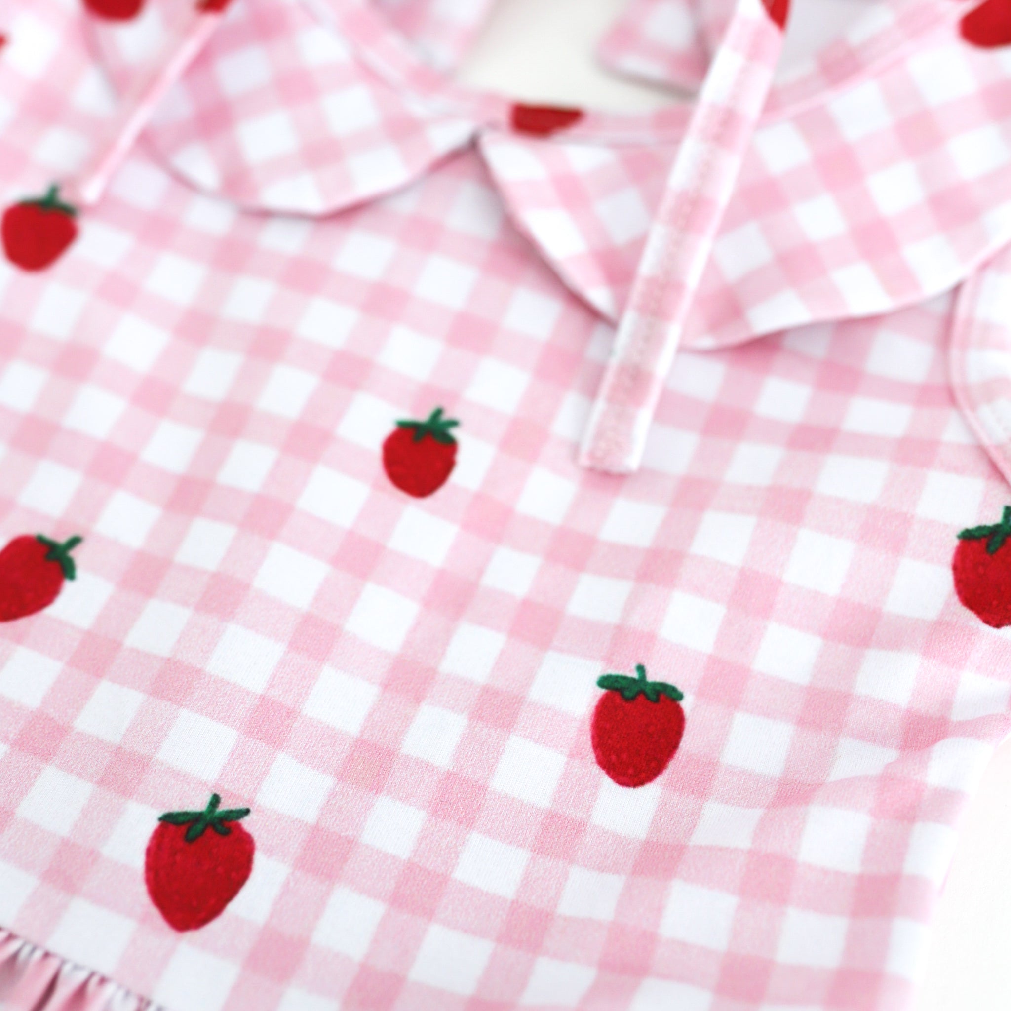detail photo of pink and white gingham print with scattered strawberries on girl's summer twirl dress