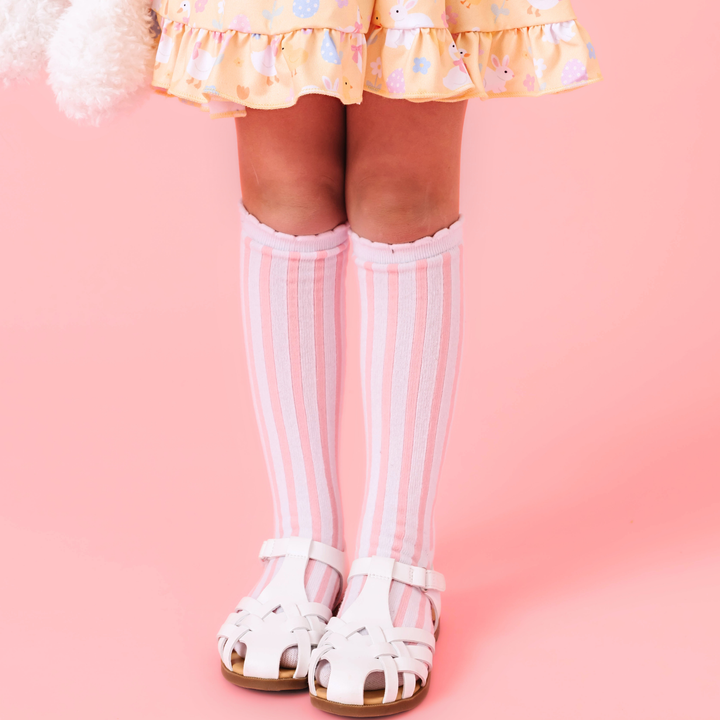 little girl in yellow Easter print dress with pink and white striped scalloped knee socks