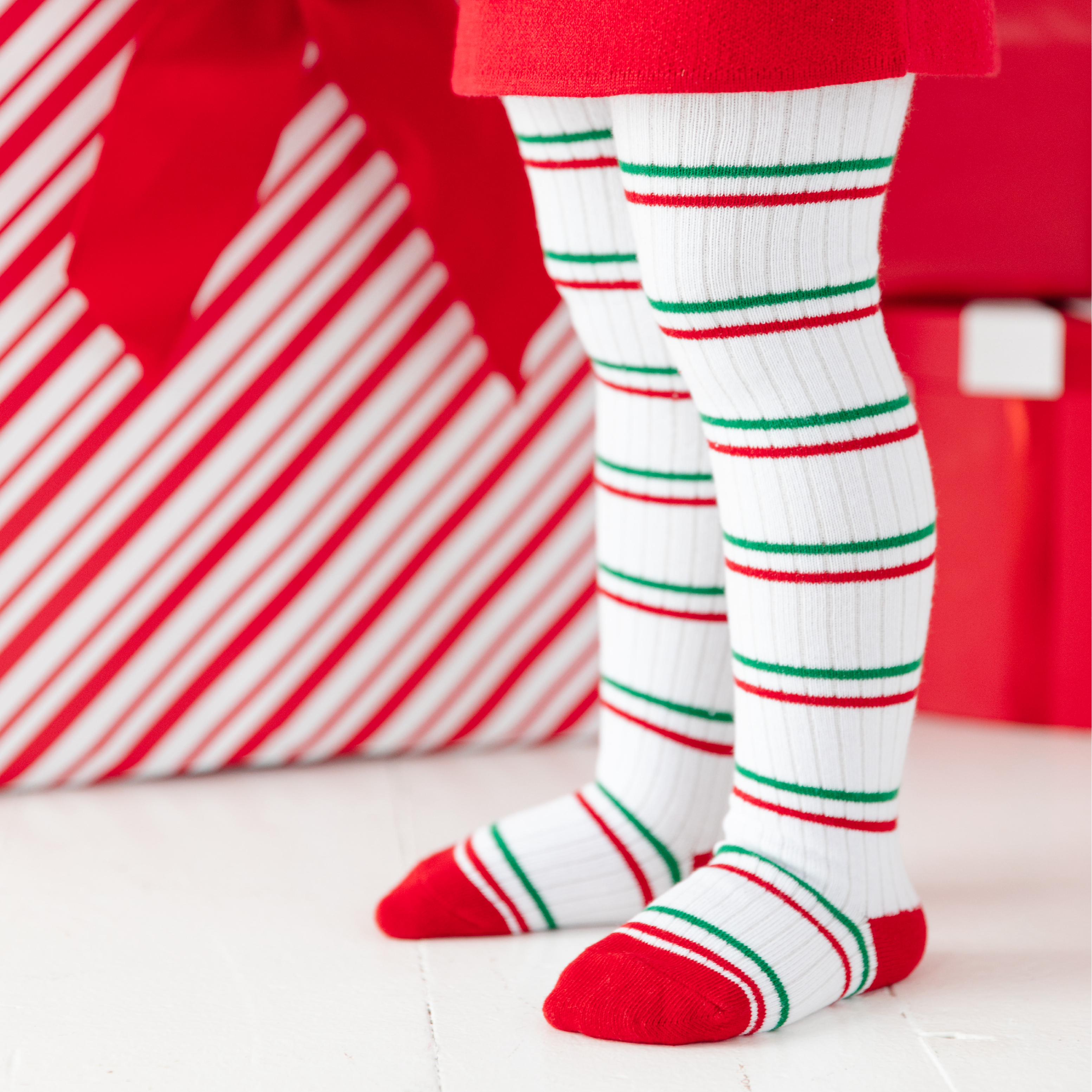 girl standing in red and green stripe tights by christmas presents