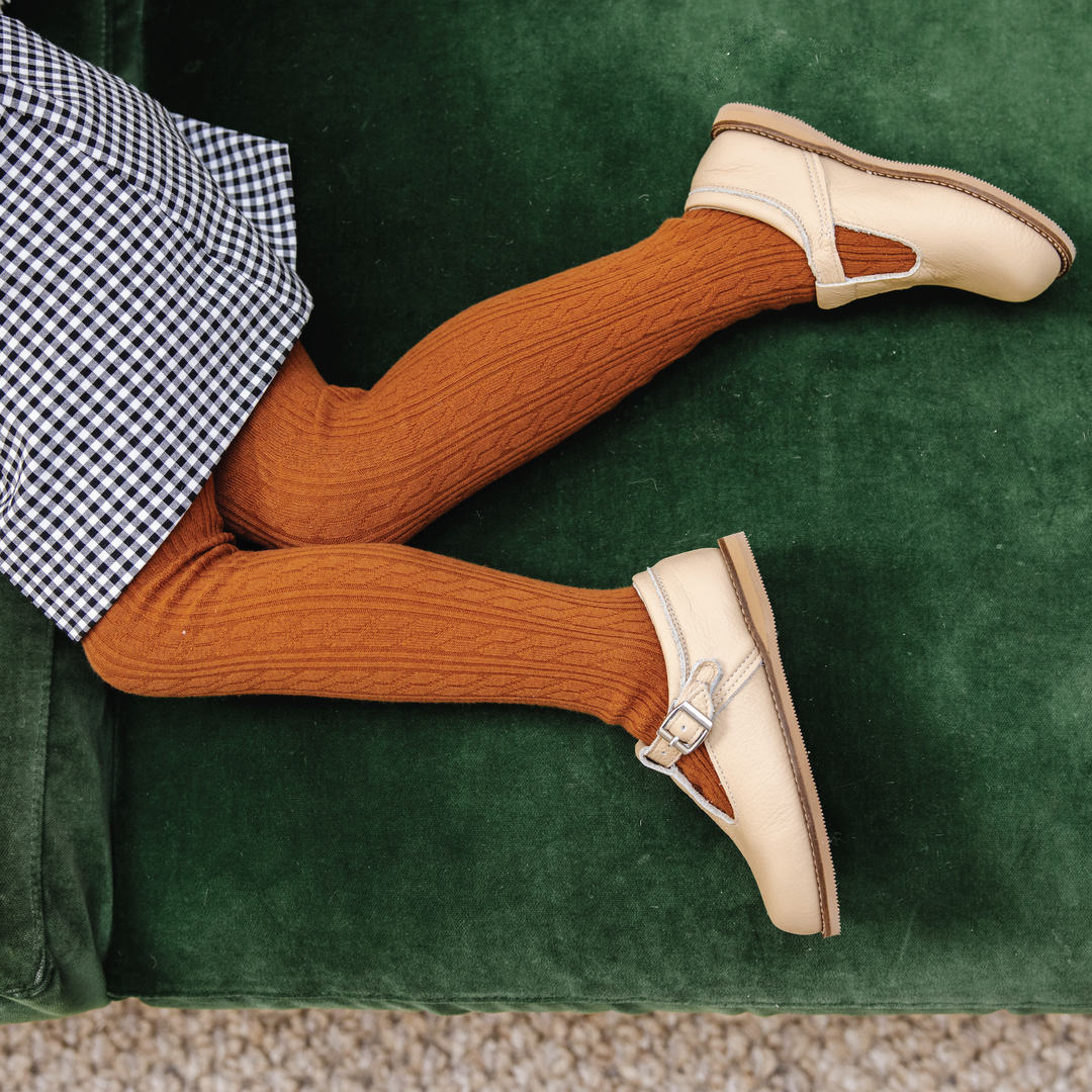 girl in sugar almond brown tights with cream leather shoes, gingham skirt, on green velvet couch