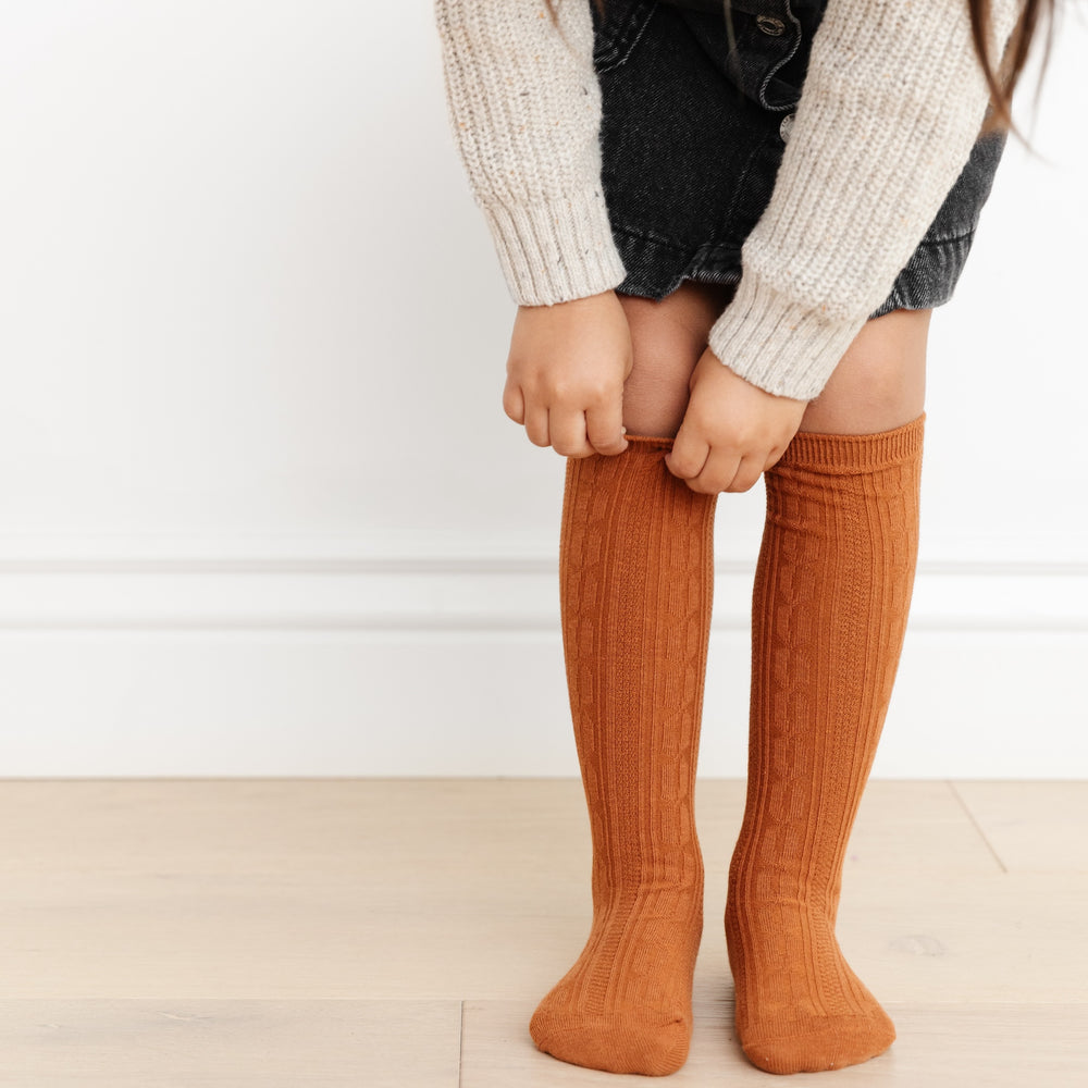 little girl pulling up cognac brown cable knit knee high socks