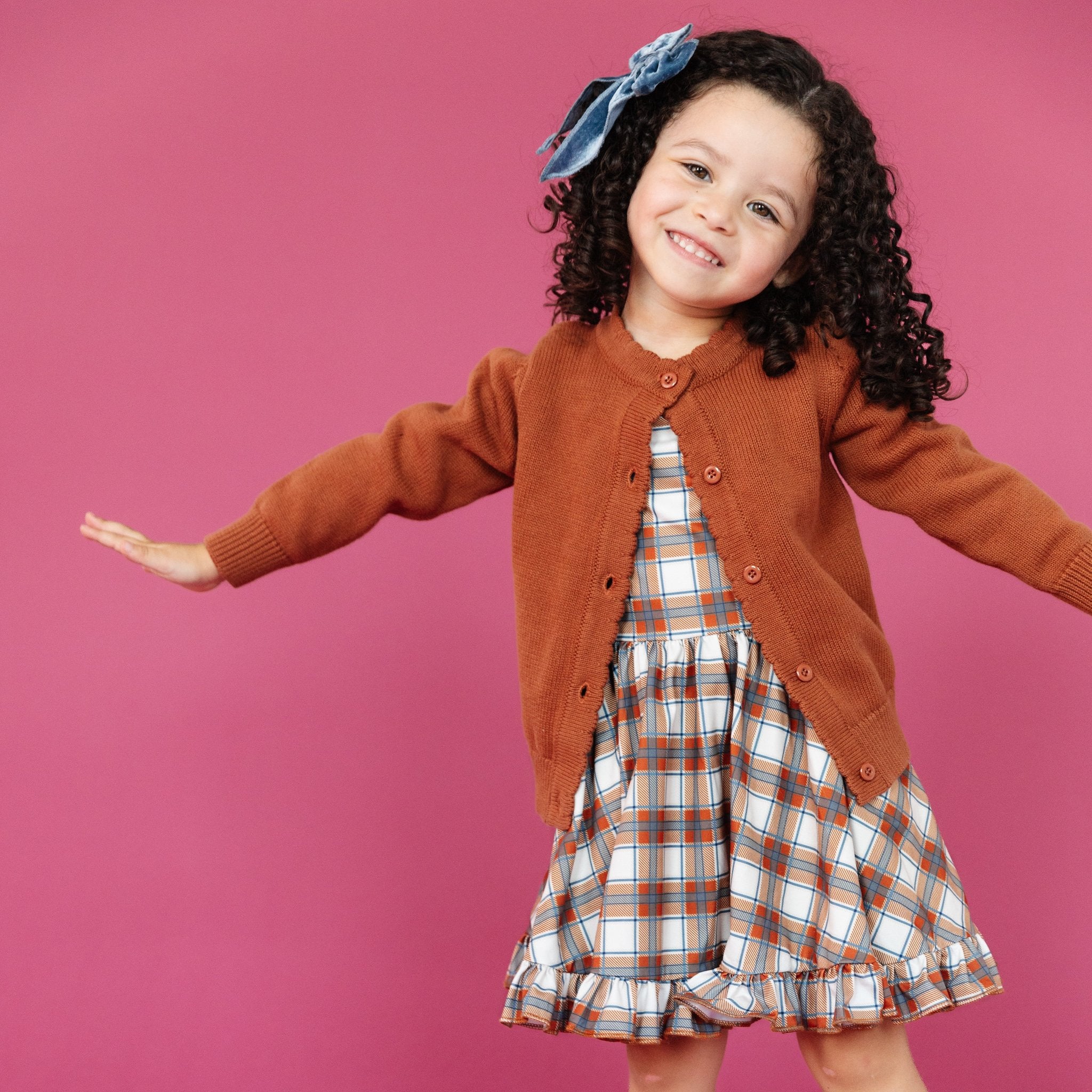 little girl in cream, blue and brown fall plaid dress with matching brown knit cardigan and blue velvet hair bow