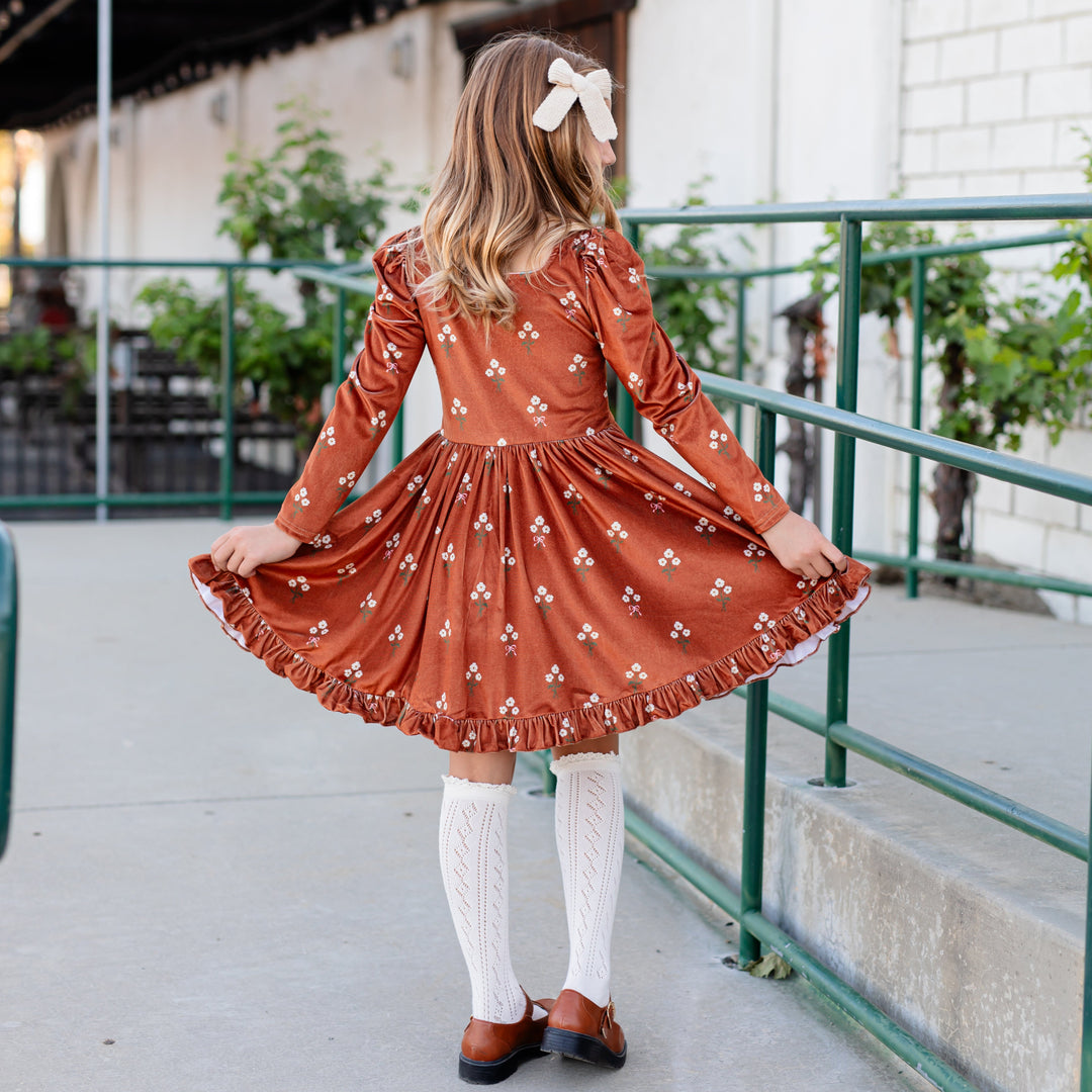 girl in long sleeve brown floral velvet twirl dress with puffed sleeve and square neck paired with light cream open knit knee socks and cream knit bow for fall