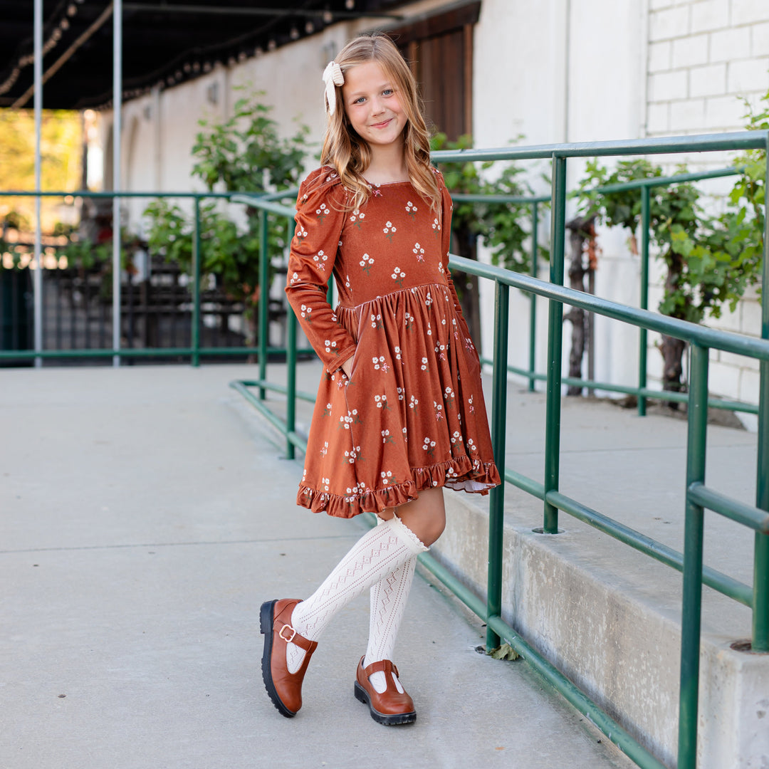 girl in rust brown long sleeve velvet twirl dress with cream floral print, ivory open knit knee high socks and cream knit hair bow for fall photos