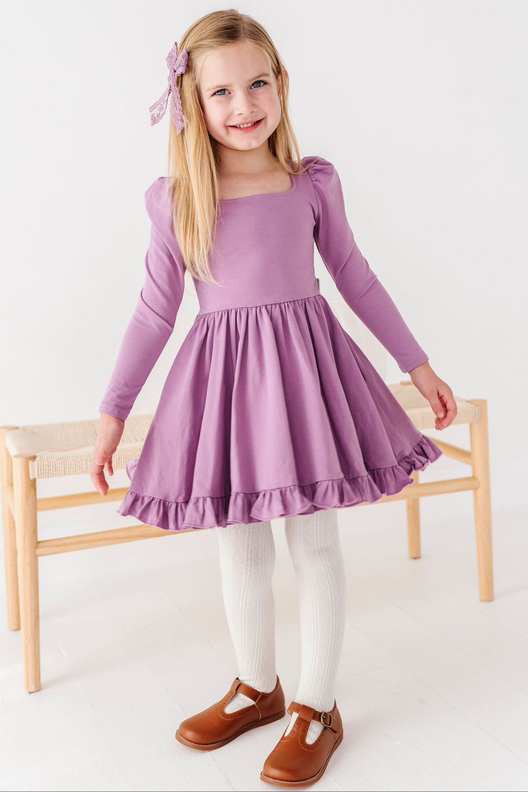 girl wearing purple long sleeve cotton twirl dress with white tights and brown t-strap shoes