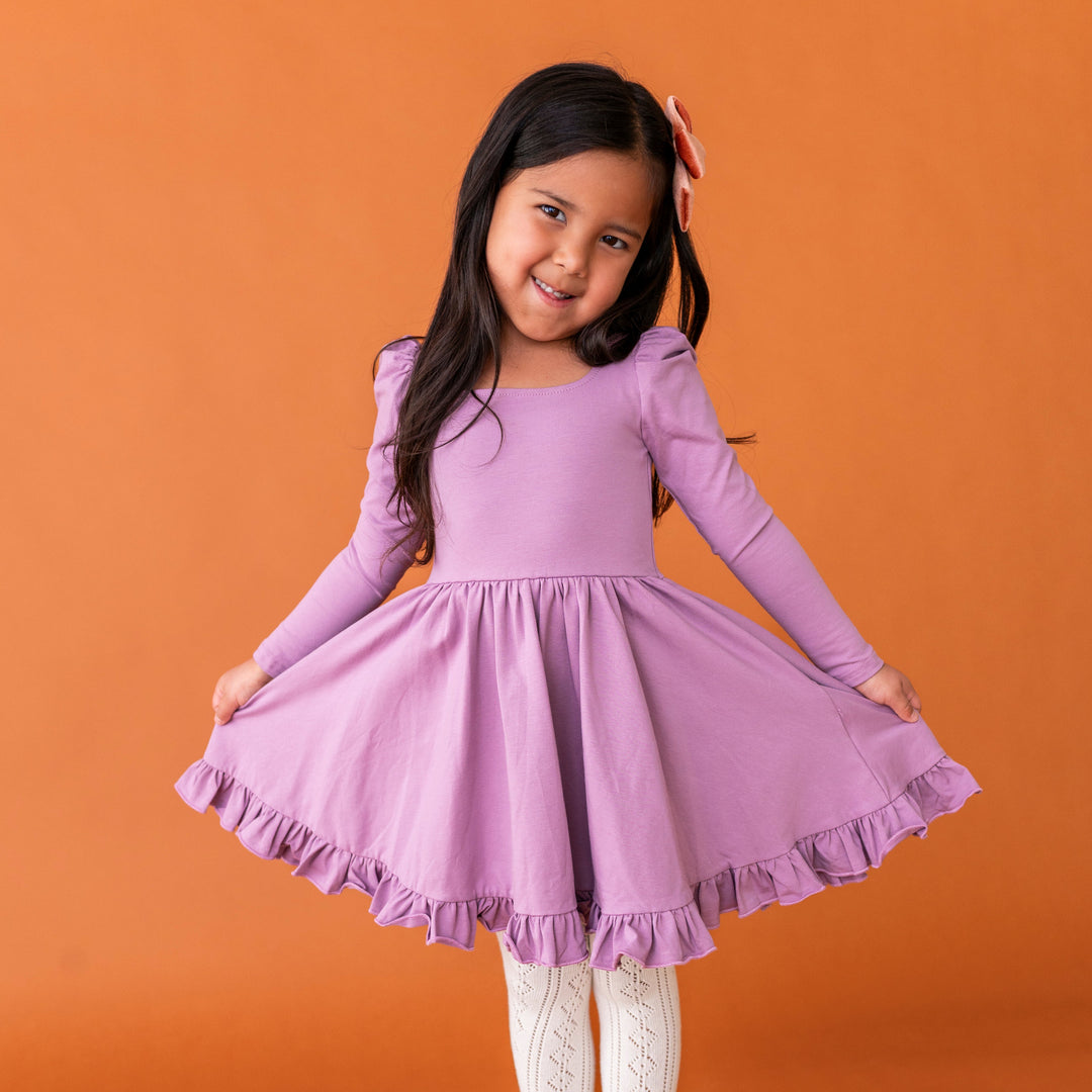 little girl posing in fall purple cotton blend twirl dress with square neckline, long sleeves and ruffled hem paired with cream pointelle tights