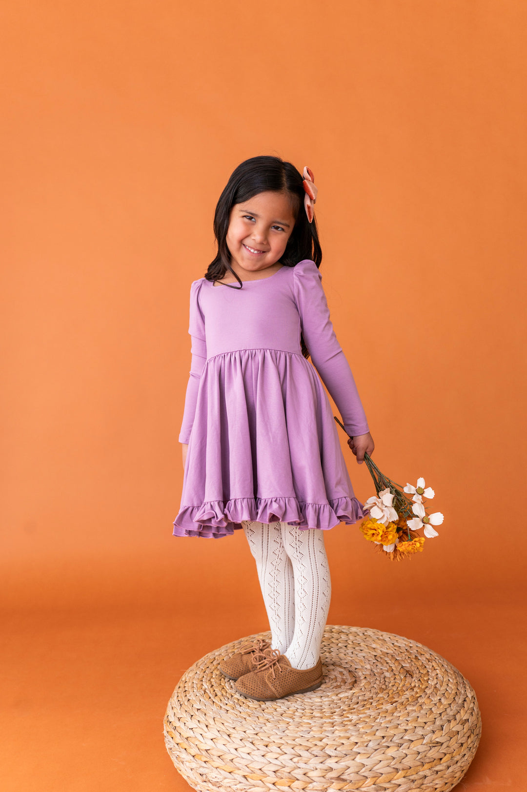 little girl holding fall flowers in purple long sleeve twirl dress paired with cream open knit tights and brown oxford shoes
