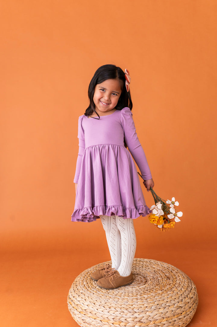 little girl holding fall flowers in purple long sleeve twirl dress paired with cream open knit tights and brown oxford shoes