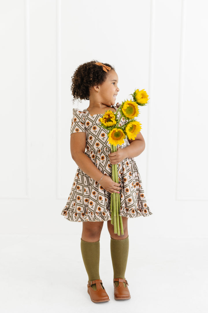 little girl holding bouquet of sunflowers in fall sunflower print twirl dress with matching olive green knee socks and mustard bow