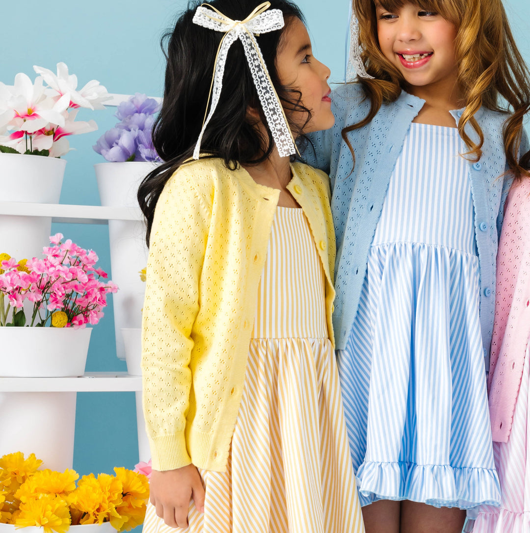 Two young girls in colorful dresses standing next to each other with a decorative background.