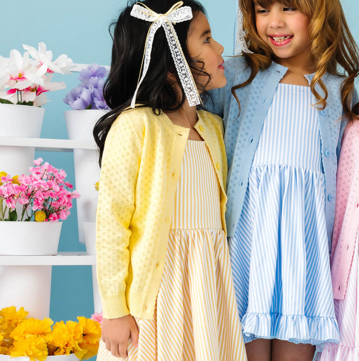 Two young girls in colorful dresses standing next to each other with a decorative background.