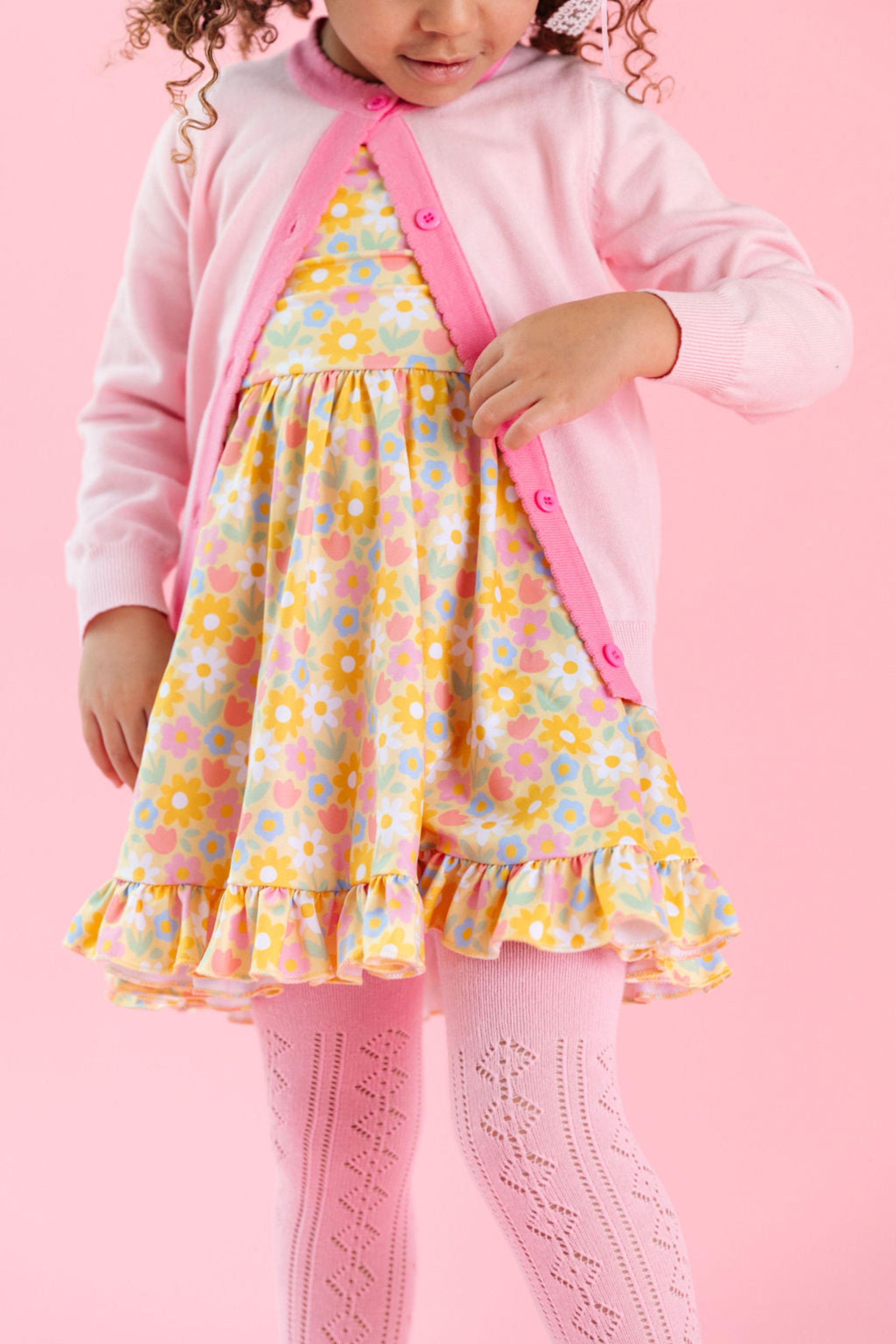 little girl in yellow spring floral twirl dress, pink pointelle tights and matching pastel pink sweater with contrast pink trim 