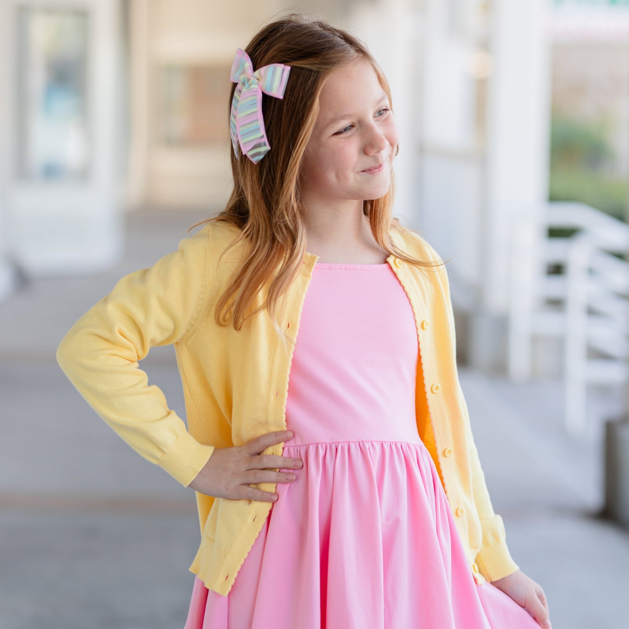 girl in spring yellow cotton knit cardigan with scallop edge detail over pink twirl dress
