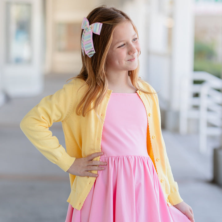 girl in spring yellow cotton knit cardigan with scallop edge detail over pink twirl dress