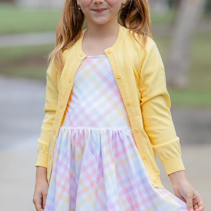 girl in spring yellow cotton knit cardigan with scallop edge detail over pastel plaid twirl dress for easter and spring