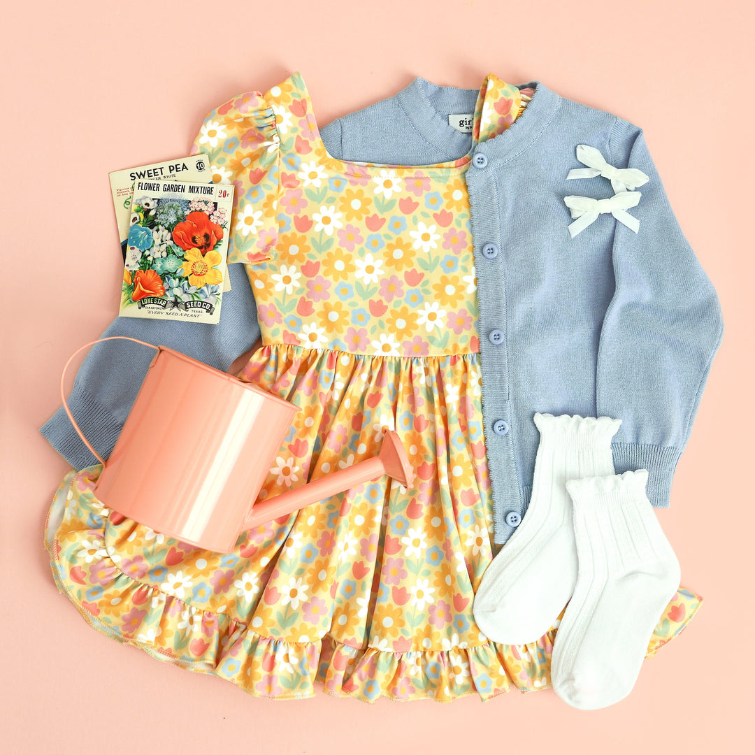 little girl's spring outfit featuring yellow floral twirl dress, blue cardigan and white midi socks and pigtail bows